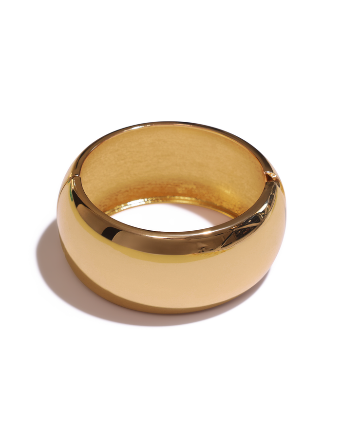The MIRAH CHUNKY BANGLE - GOLD by TIGERMIST is a thick, shiny gold bangle with a smooth, rounded surface—resembling a chunky bracelet—and casts a soft shadow on a white background.