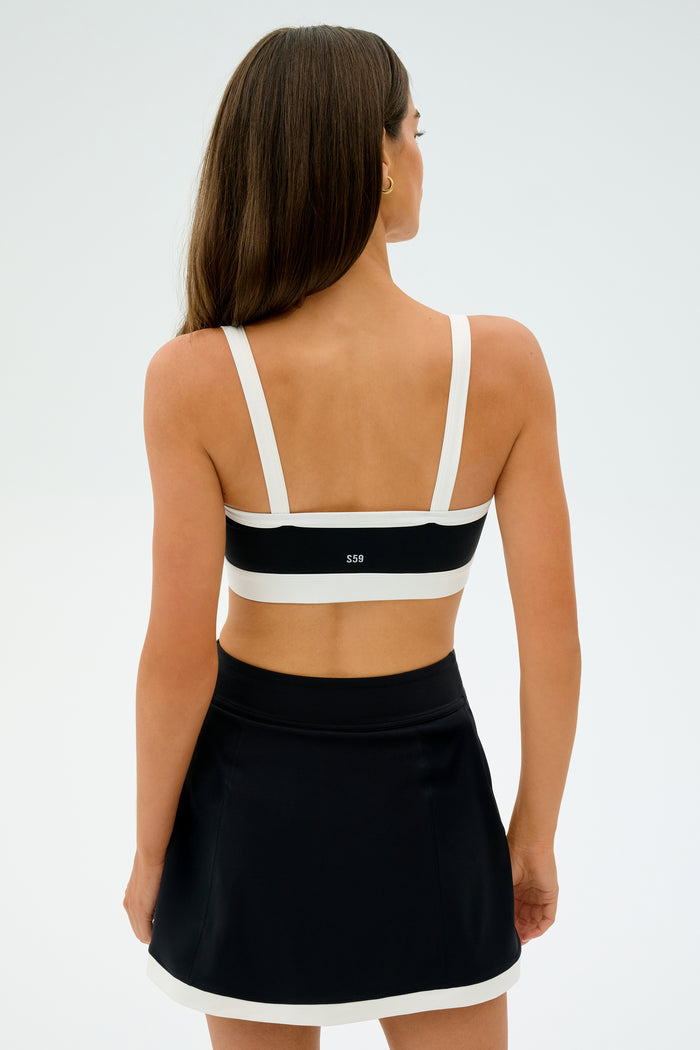 A person with long hair is facing away, wearing a SPLITS59 Monah Rigor Bra in Black/White that exudes a retro sports vibe paired with a black skirt.