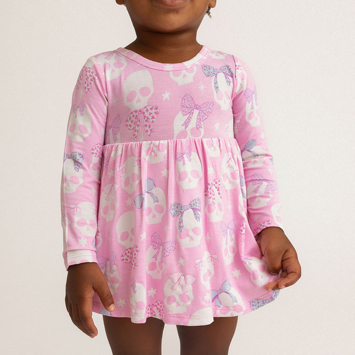 Child standing, wearing the Posh Peanut Ms. Kelly Bow Back Bodysuit Dress, white background