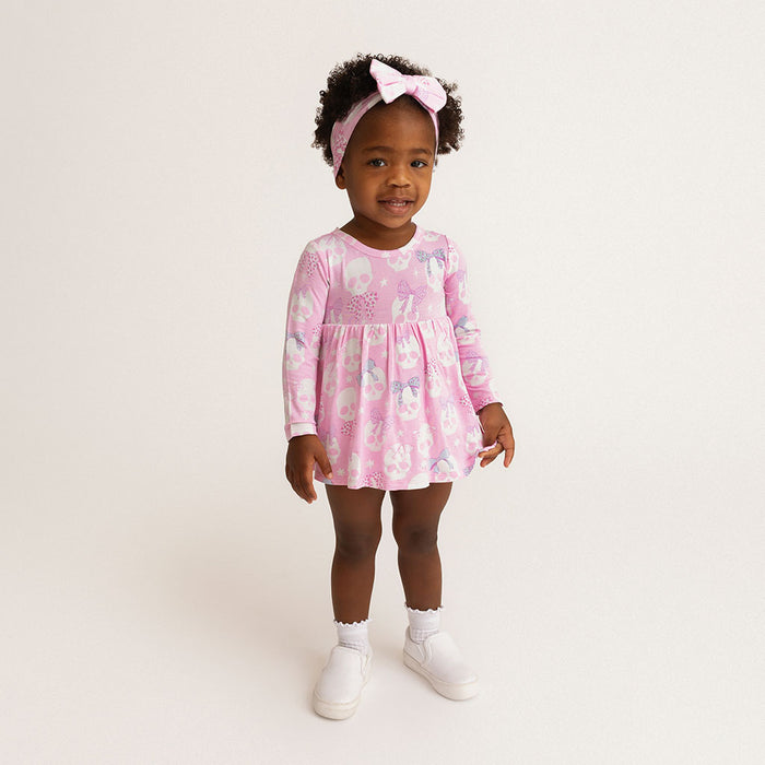 Child standing, wearing the Posh Peanut Ms. Kelly Bow Back Bodysuit Dress, white background