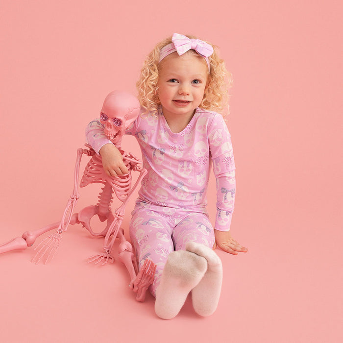 Child sitting, wearing the Posh Peanut Ms. Kelly Classic Pajama Set, pink background