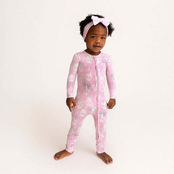 Child standing, wearing the Posh Peanut Ms. Kelly Convertible One Piece, hair bow, white background