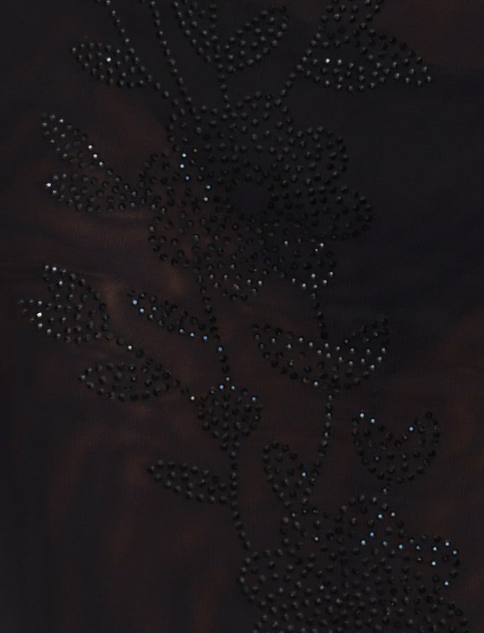 Close-up of the fabric from the OCTAVIA DRESS - BLACK by TIGERMIST, showcasing intricate floral patterns created by small, shiny black beads. The beads form delicate outlines and details of flowers and leaves, giving the dress an elegant, textured appearance. The background fabric appears to be semi-sheer.