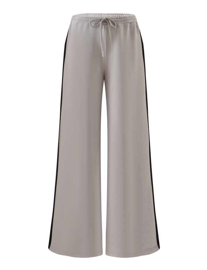 The PAYTON TRACKPANT - STONE by TIGERMIST features a wide-leg fit, light gray cotton fabric, an elastic drawstring waistband, and black side stripes, shown against a plain white background.
