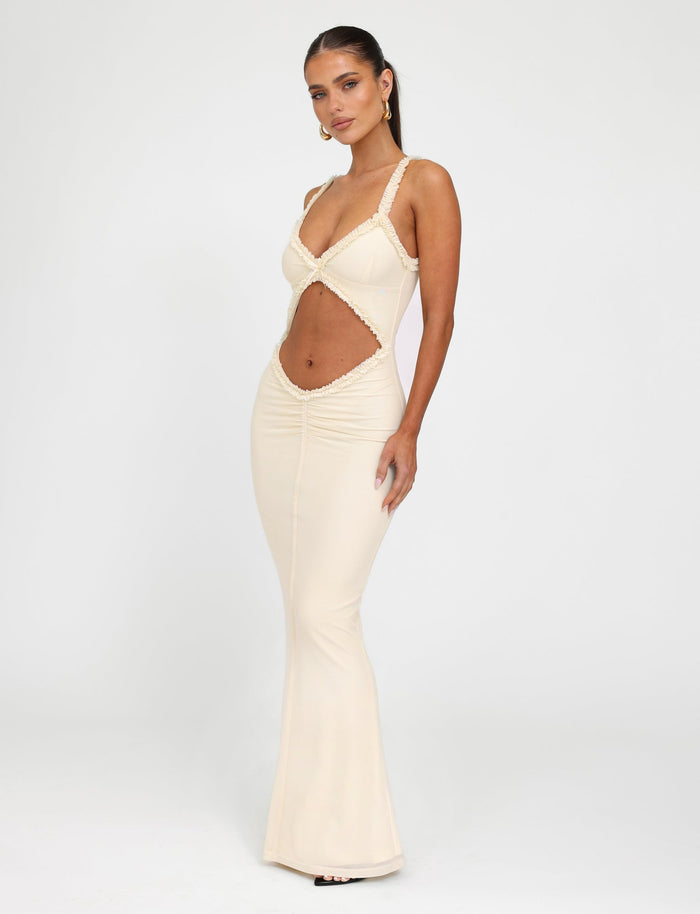 Against a plain white background, a woman models the sleek RAYLA DRESS - WHITE : CREAM by TIGERMIST. This form-fitting, sleeveless dress features cut-out detailing at the midsection and a plunging neckline. Its mermaid silhouette elegantly highlights her figure as she poses with one hand on her hip.