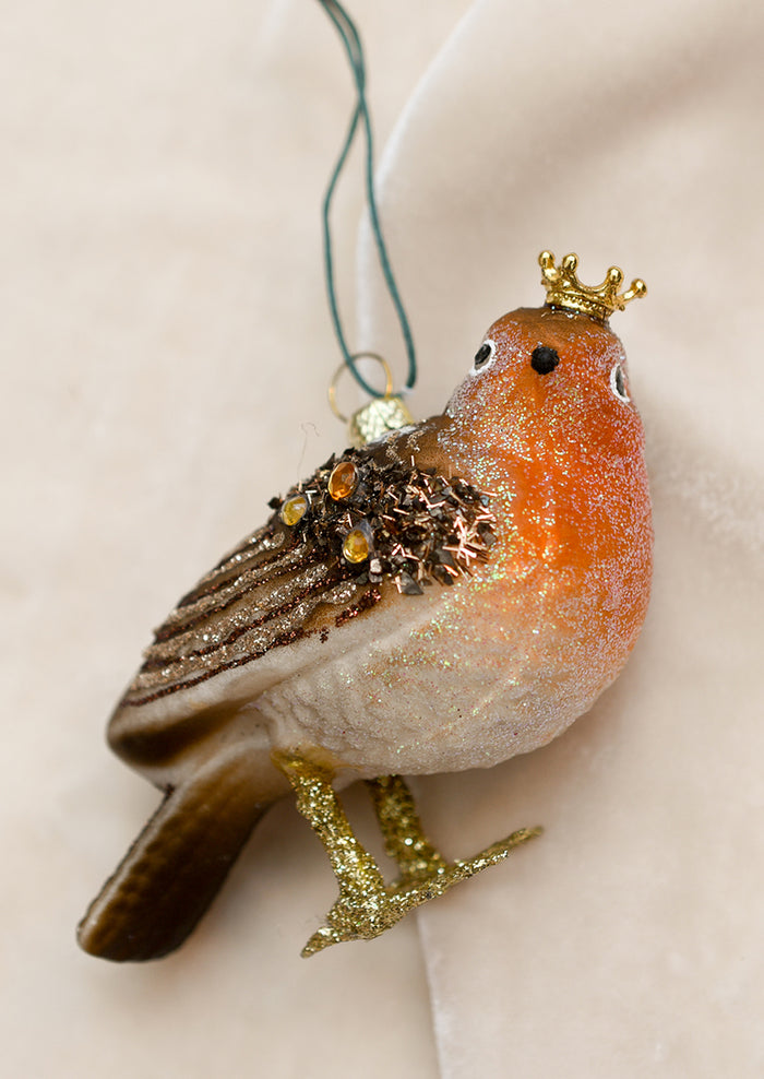 A glass holiday ornament of a glittery robin wearing a gold crown.