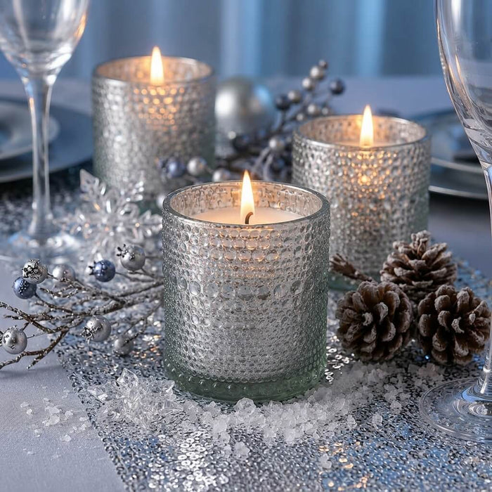 Pearly silver candle holders with winter decor and glowing candles on a festive table