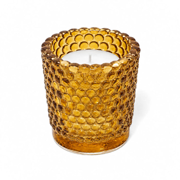 Amber hobnail glass votive candle holder with white candle on white background