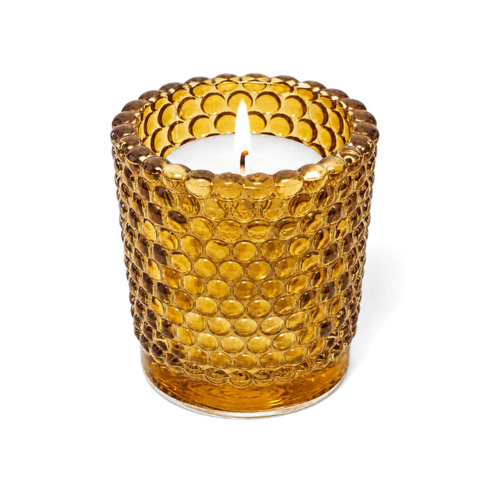 Amber hobnail glass votive candle holder with lit white candle on white background