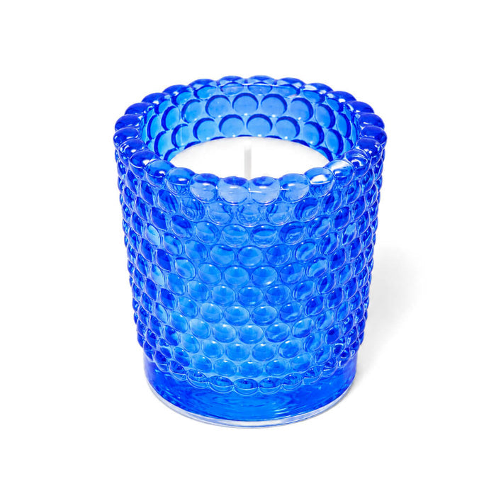 Blue hobnail glass votive candle holder with white candle on white background