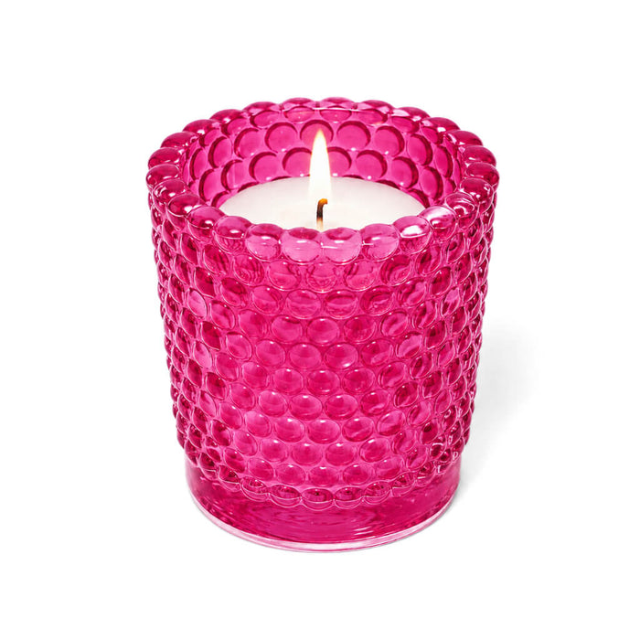 Pink hobnail glass votive holder with lit candle on white background