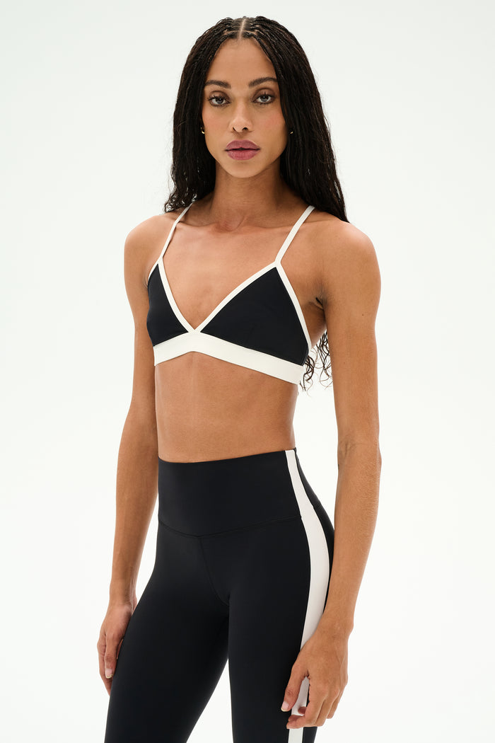 A person stands against a plain white background wearing the SPLITS59 Sage Rigor Bra in black and white, paired with matching high-waisted leggings, both crafted from a comfortable blend of nylon and spandex.