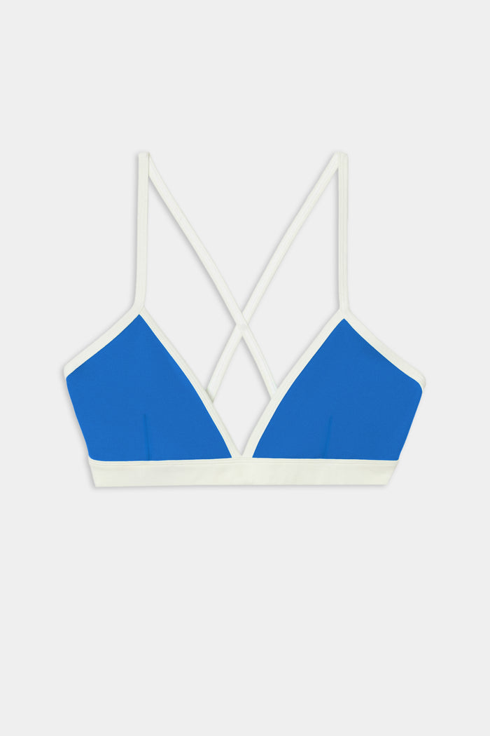 SPLITS59 Sage Rigor Bra in Classic Blue/White, a bralette-style top crafted from soft nylon spandex fabric, features white straps and trim with a crisscross back design, showcased against a plain white background.