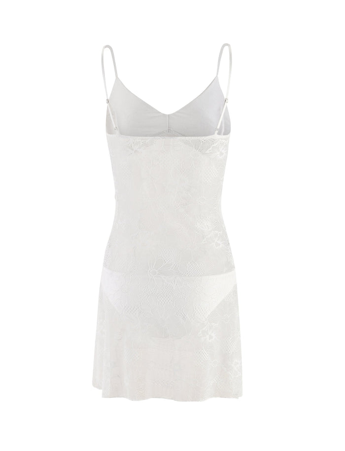The SASKIA DRESS - WHITE by TIGERMIST is a white lace lingerie dress with thin shoulder straps. It features a fitted bust area and a flowy, semi-sheer skirt adorned with a floral pattern. The delicate lace design adds an elegant and feminine touch.