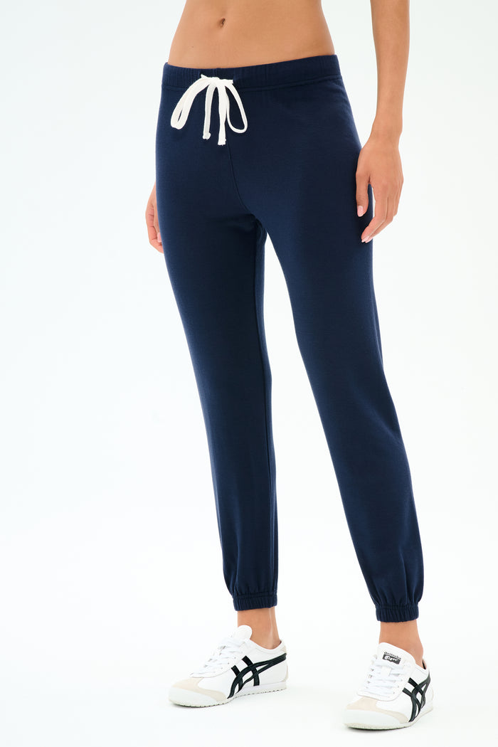 A person in SPLITS59 Sonja Fleece Sweatpant - Indigo, featuring slouchy-soft ultra luxe fleece and a white drawstring, paired with white sneakers, stands against a plain white background.