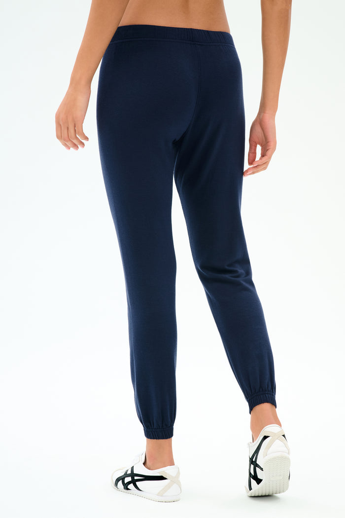Model wears the SPLITS59 Sonja Fleece Sweatpant in Indigo with white sneakers, shown from the back against a plain white background. Made in Los Angeles from ultra luxe fleece for ultimate comfort and style.