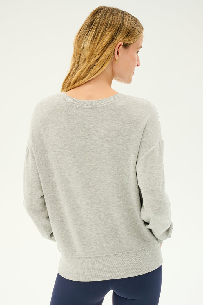 A person with long blonde hair is seen from behind, wearing the SPLITS59 Sonja Fleece Sweatshirt in Heather Grey and black leggings made in Los Angeles, standing against a plain white background.