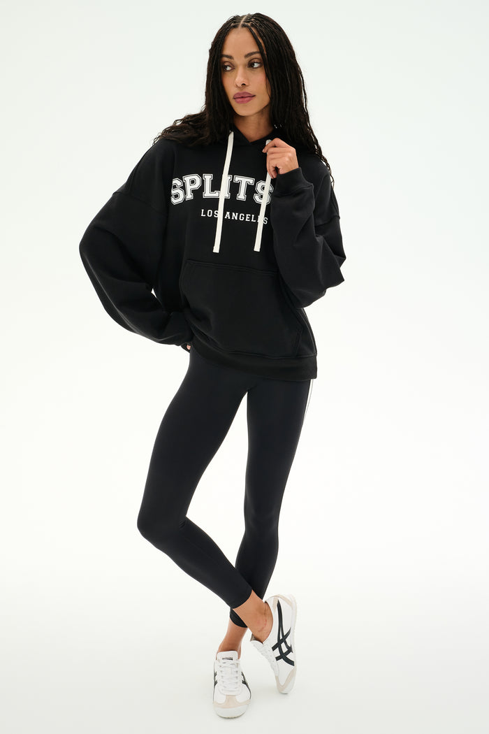 A person stands against a plain white background wearing the SPLITS59 Stella French Terry Oversized Hoodie in black, paired with black leggings and white sneakers.