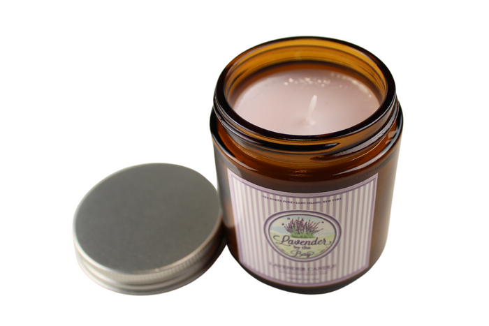 A small, round large glass jar scented candle with a pink wax and a silver lid. The jar has a label with the words "Lavender by the Bay