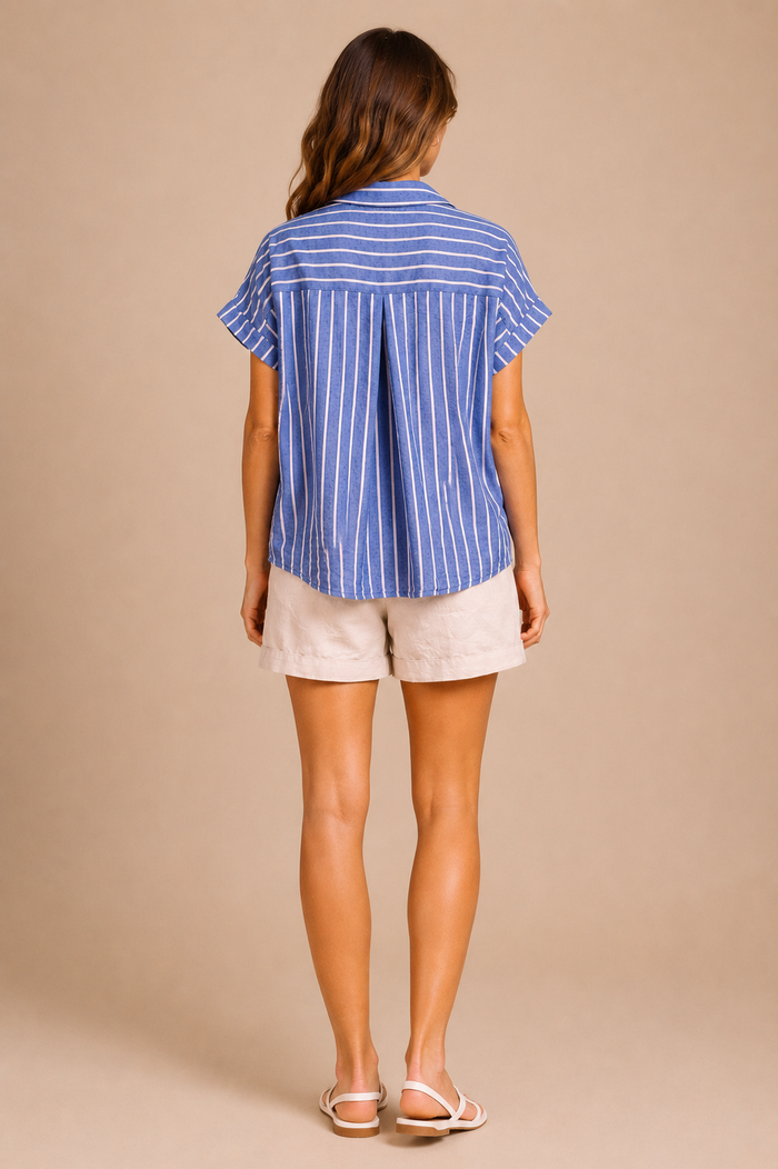 Woman wearing a blue striped shirt and white shorts against a beige background